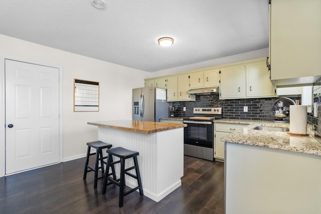 kitchen with a kitchen island, under cabinet range hood, cream cabinets, stainless steel appliances, and a sink