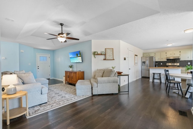 living room featuring a ceiling fan, visible vents, dark wood-style floors, baseboards, and a textured ceiling