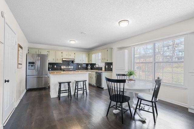 kitchen with under cabinet range hood, a center island, stainless steel appliances, light countertops, and decorative backsplash