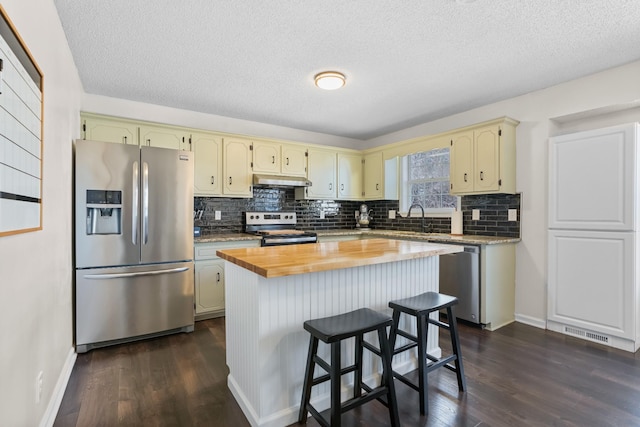 kitchen featuring cream cabinetry, butcher block counters, stainless steel appliances, and dark wood-type flooring