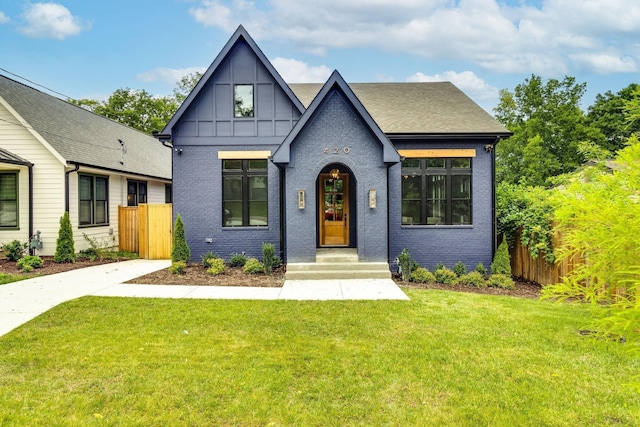 english style home featuring brick siding, a shingled roof, a front lawn, and fence