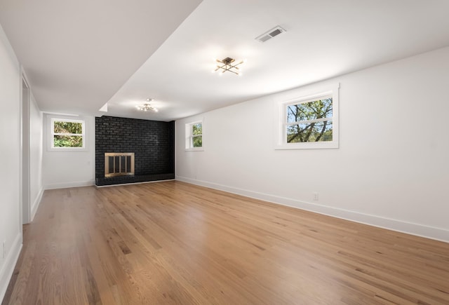 unfurnished living room featuring visible vents, light wood-style flooring, a brick fireplace, and baseboards