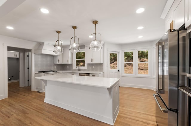 kitchen featuring custom exhaust hood, a sink, light countertops, light wood-style floors, and appliances with stainless steel finishes