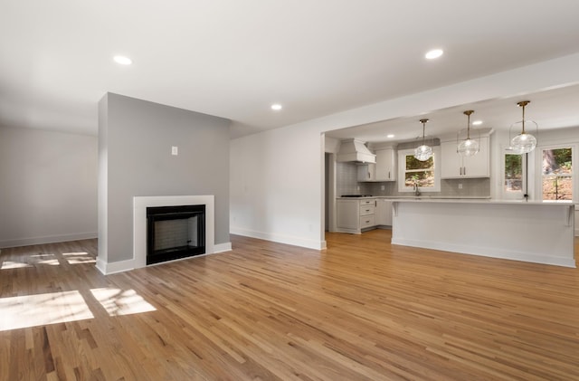 unfurnished living room featuring baseboards, recessed lighting, a fireplace, light wood-style floors, and a sink