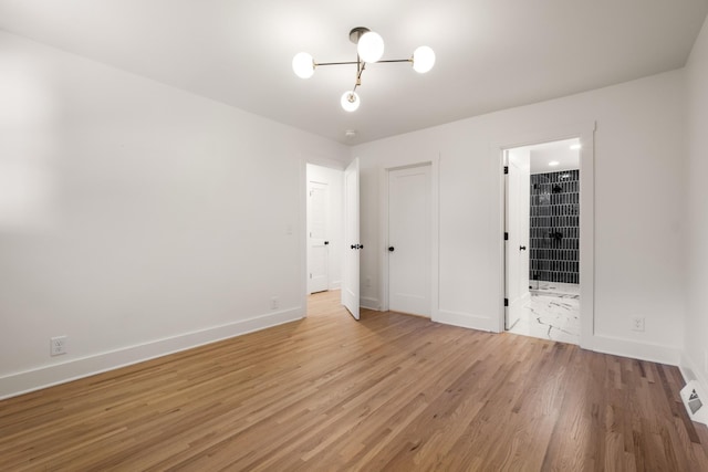 unfurnished bedroom with connected bathroom, baseboards, and light wood-style floors