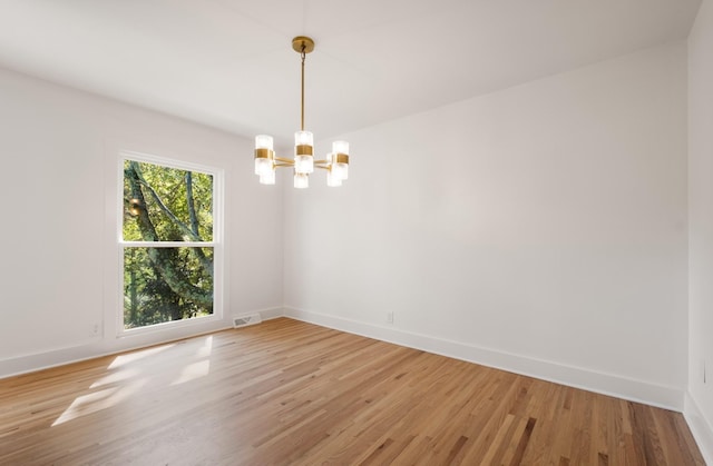 unfurnished room featuring light wood-type flooring, baseboards, visible vents, and a chandelier