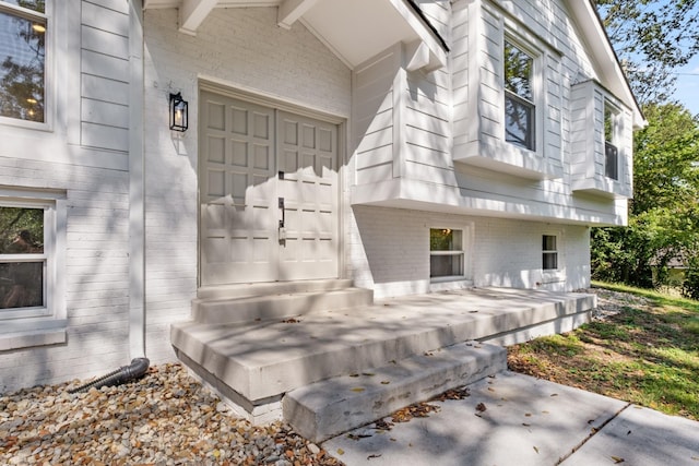 view of exterior entry featuring a garage and brick siding