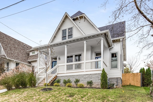 view of front of house featuring a porch, roof with shingles, a front yard, and fence