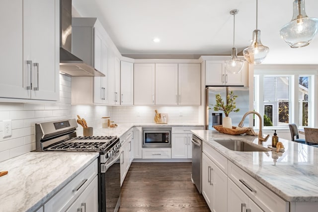 kitchen featuring wall chimney range hood, decorative backsplash, stainless steel appliances, white cabinetry, and a sink