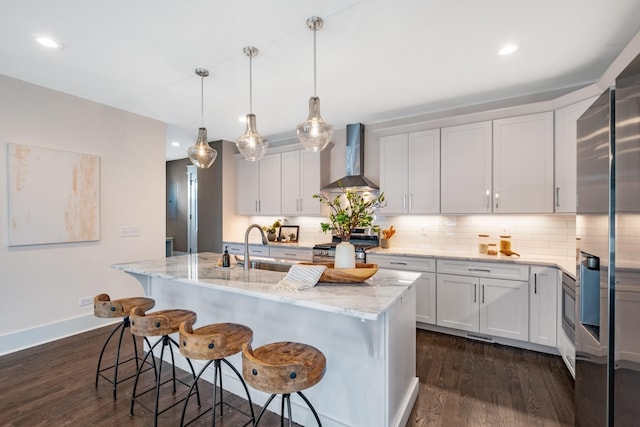 kitchen featuring a kitchen bar, appliances with stainless steel finishes, wall chimney exhaust hood, decorative backsplash, and dark wood-style flooring