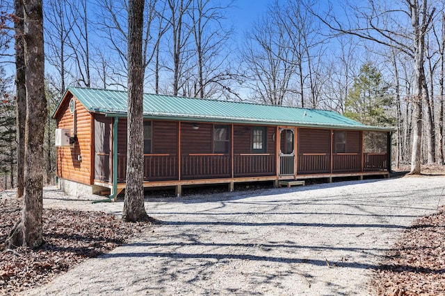 view of front of house with faux log siding, a porch, driveway, and metal roof