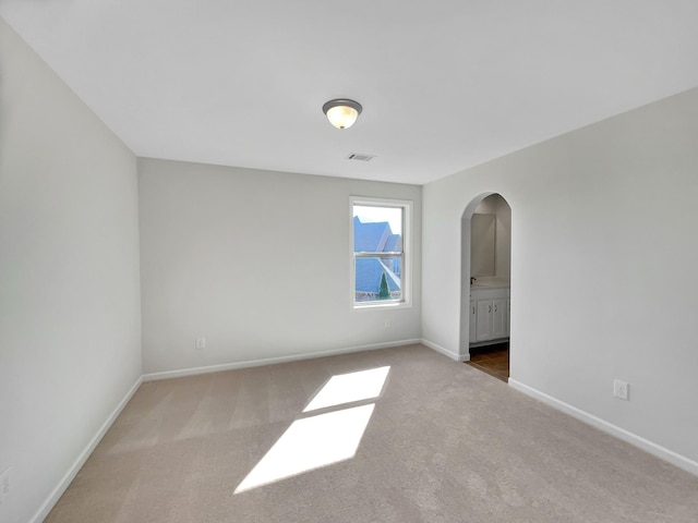 carpeted spare room with visible vents, arched walkways, and baseboards