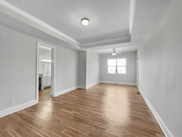 spare room featuring a ceiling fan, baseboards, a tray ceiling, ornamental molding, and light wood-type flooring