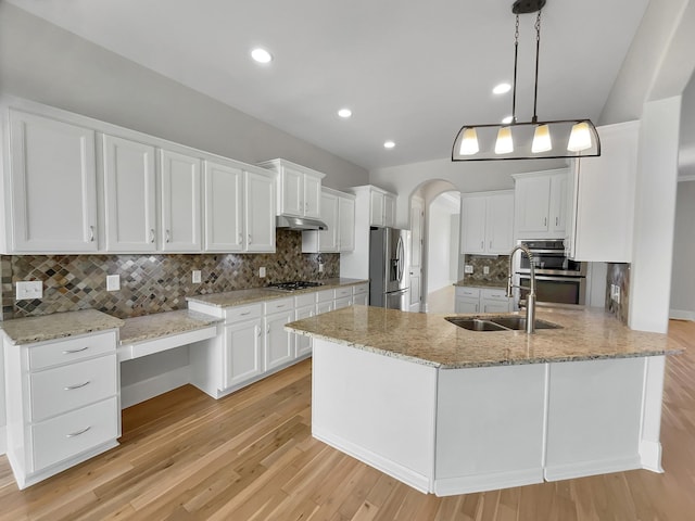 kitchen featuring under cabinet range hood, appliances with stainless steel finishes, arched walkways, white cabinets, and a sink