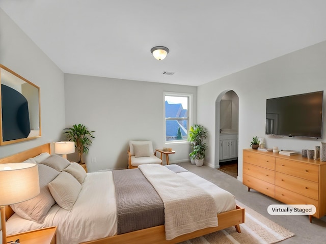 carpeted bedroom featuring arched walkways, visible vents, ensuite bathroom, and baseboards