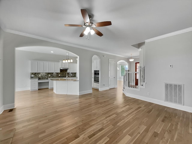 unfurnished living room featuring light wood-type flooring, visible vents, arched walkways, and baseboards