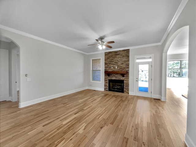 unfurnished living room featuring ornamental molding, arched walkways, light wood-style floors, a stone fireplace, and baseboards