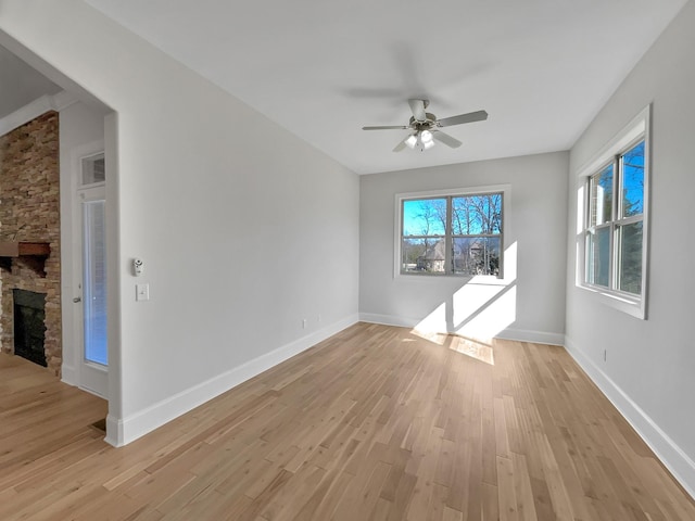 spare room featuring a stone fireplace, light wood-style flooring, baseboards, and ceiling fan