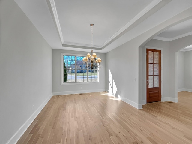 unfurnished dining area with ornamental molding, an inviting chandelier, light wood-style floors, arched walkways, and a raised ceiling