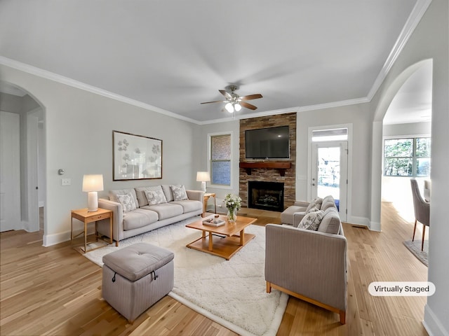 living room featuring light wood finished floors, arched walkways, a fireplace, crown molding, and baseboards