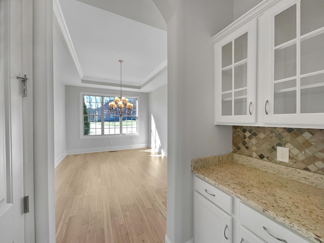 kitchen with an inviting chandelier, decorative backsplash, glass insert cabinets, white cabinetry, and a raised ceiling