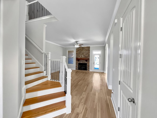 foyer with light wood finished floors, a ceiling fan, a fireplace, crown molding, and stairs