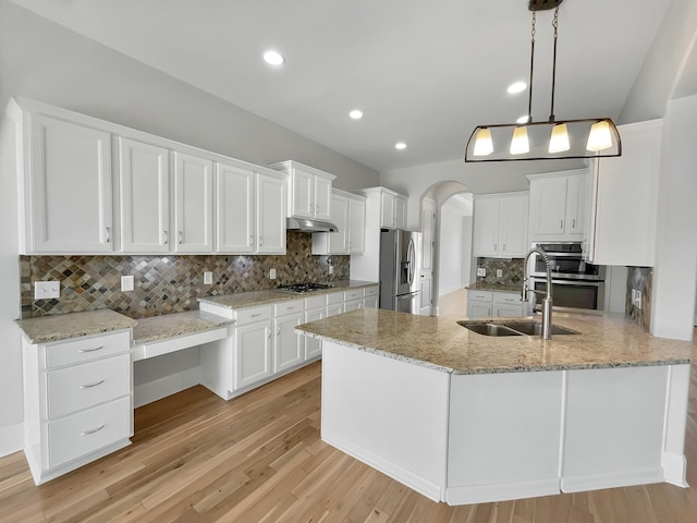 kitchen with under cabinet range hood, arched walkways, white cabinets, stainless steel appliances, and a sink