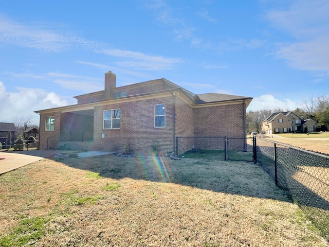 view of property exterior featuring brick siding, a chimney, a yard, and fence