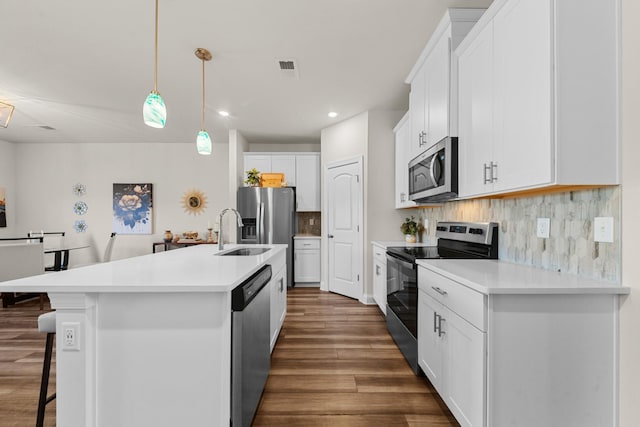 kitchen featuring an island with sink, backsplash, dark wood-style floors, appliances with stainless steel finishes, and light countertops