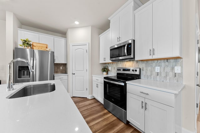 kitchen featuring a sink, wood finished floors, stainless steel appliances, white cabinets, and light countertops