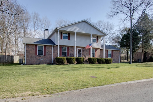 view of front facade featuring a front yard, cooling unit, fence, a chimney, and brick siding