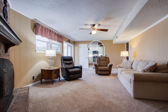 living area featuring crown molding, carpet, arched walkways, and ceiling fan