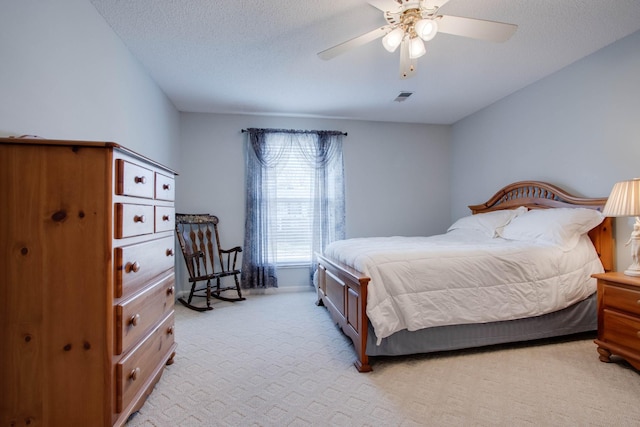 bedroom with visible vents, light carpet, a textured ceiling, and a ceiling fan