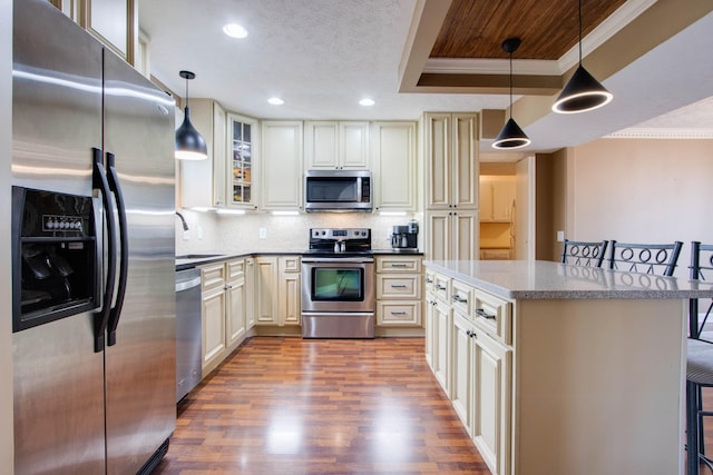 kitchen featuring backsplash, appliances with stainless steel finishes, wood finished floors, a raised ceiling, and a sink