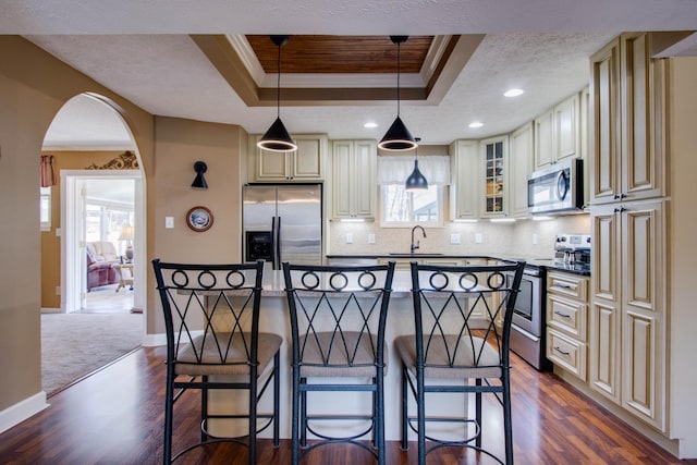 kitchen featuring a sink, stainless steel appliances, cream cabinetry, crown molding, and a raised ceiling