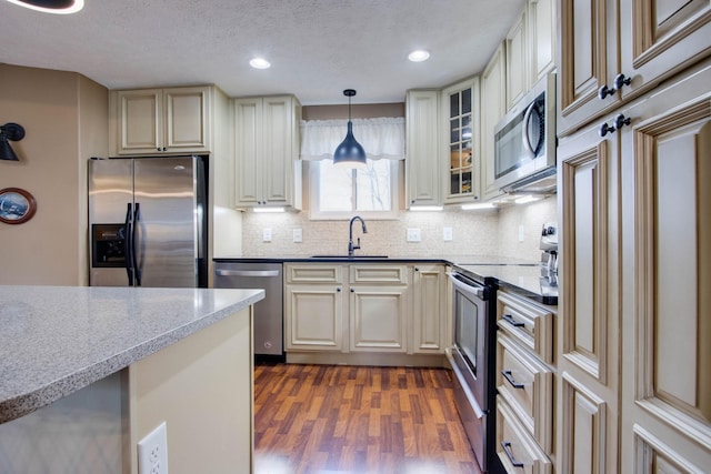 kitchen featuring a sink, tasteful backsplash, dark wood-style floors, appliances with stainless steel finishes, and hanging light fixtures