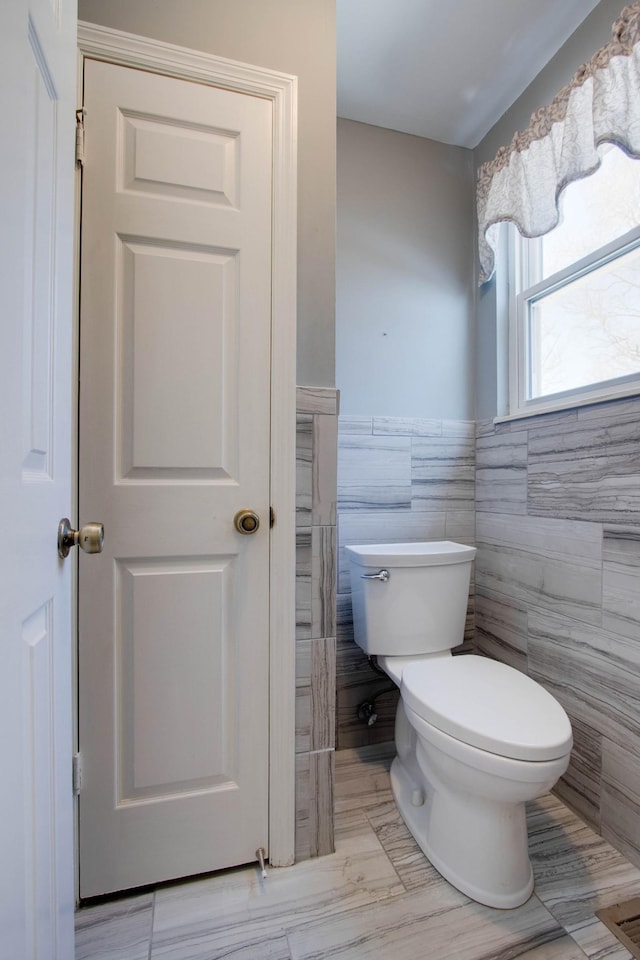 bathroom featuring wainscoting, toilet, and tile walls