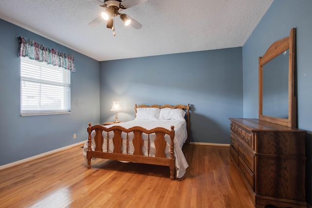 bedroom featuring a ceiling fan, wood finished floors, baseboards, and a textured ceiling