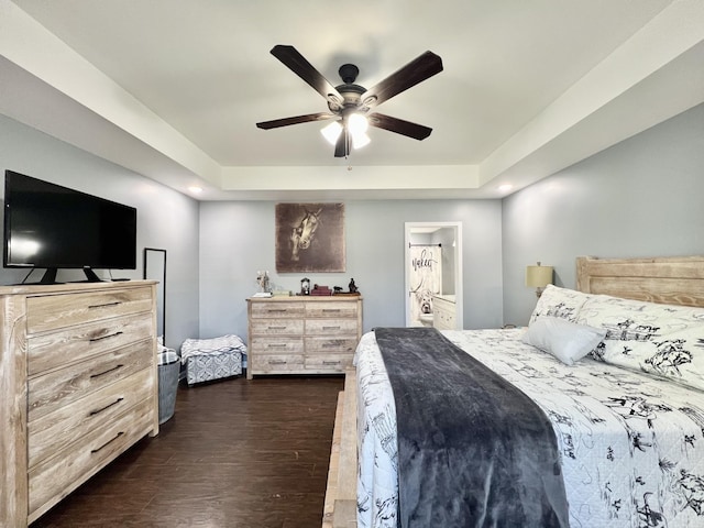 bedroom with ensuite bath, dark wood-type flooring, a ceiling fan, and a raised ceiling