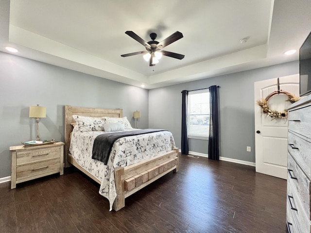 bedroom featuring a tray ceiling, baseboards, and dark wood-type flooring