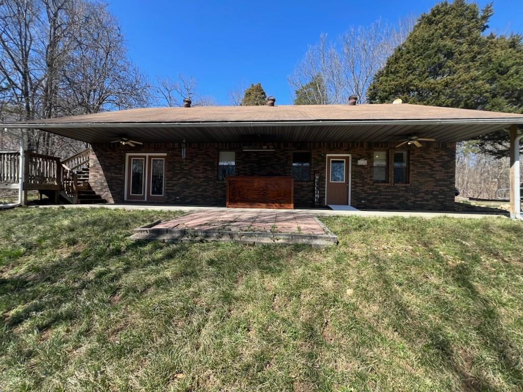 back of house with brick siding, a lawn, stairs, and ceiling fan