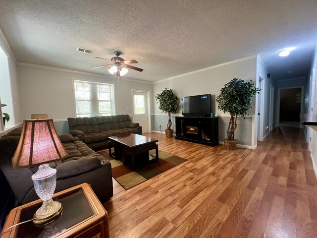 living room with a ceiling fan, crown molding, wood finished floors, and a textured ceiling