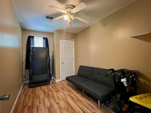 living area with ceiling fan, light wood finished floors, a textured ceiling, and visible vents