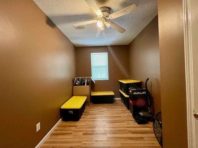 interior space with a textured ceiling, light wood finished floors, baseboards, and a ceiling fan