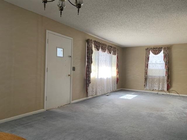 carpeted entrance foyer with a notable chandelier, plenty of natural light, baseboards, and a textured ceiling