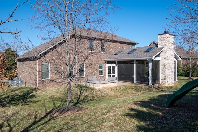 back of house featuring a yard, brick siding, a sunroom, and a chimney