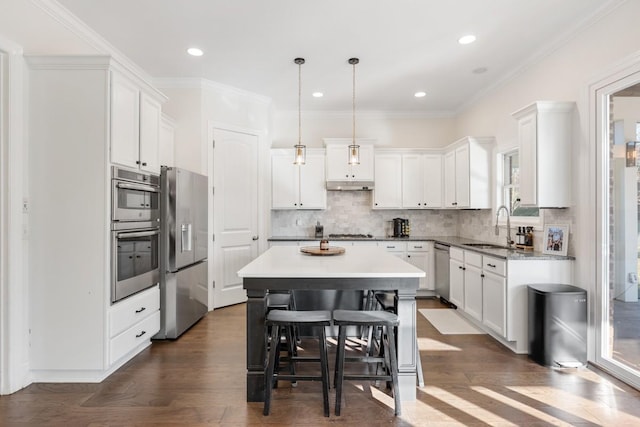 kitchen with a kitchen island, dark wood-type flooring, under cabinet range hood, appliances with stainless steel finishes, and a sink