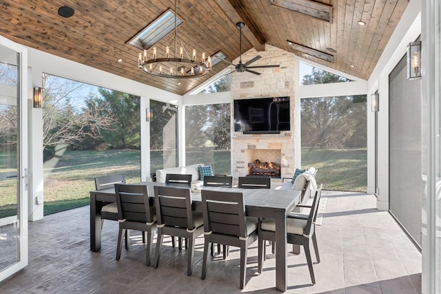 sunroom / solarium featuring a large fireplace, ceiling fan with notable chandelier, wooden ceiling, and lofted ceiling with beams