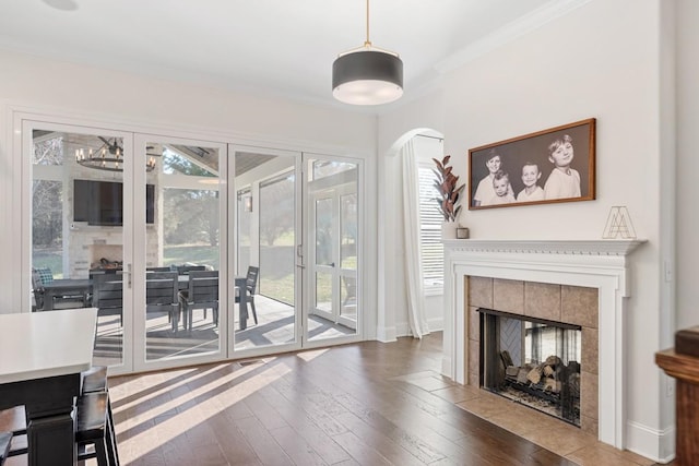 living room featuring a tiled fireplace, a healthy amount of sunlight, ornamental molding, and hardwood / wood-style floors