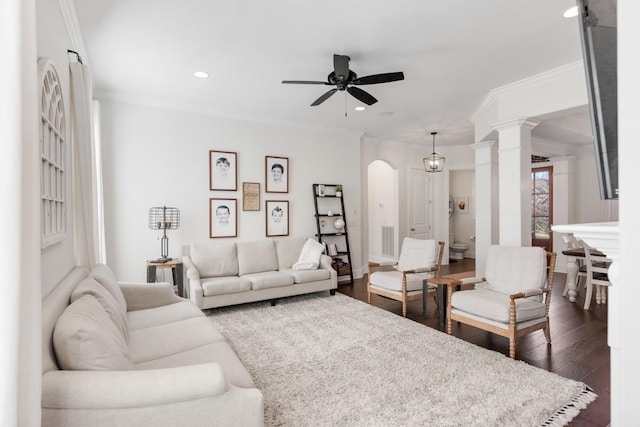 living area featuring ceiling fan, decorative columns, dark wood finished floors, and crown molding